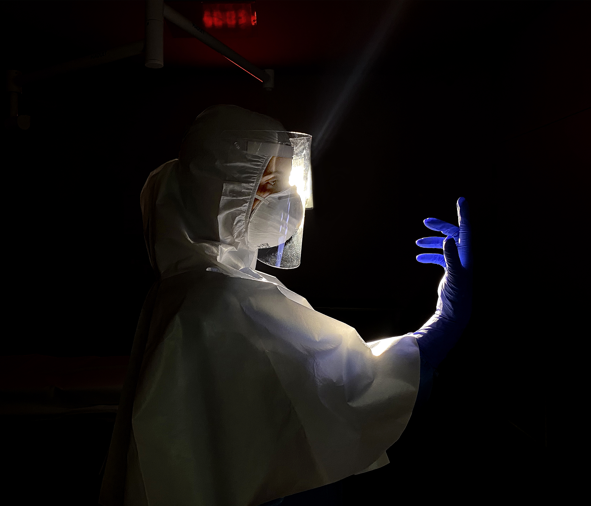 Enfermeira de perfil em ambiente escuro com mão direita elevada usando luva roxa.