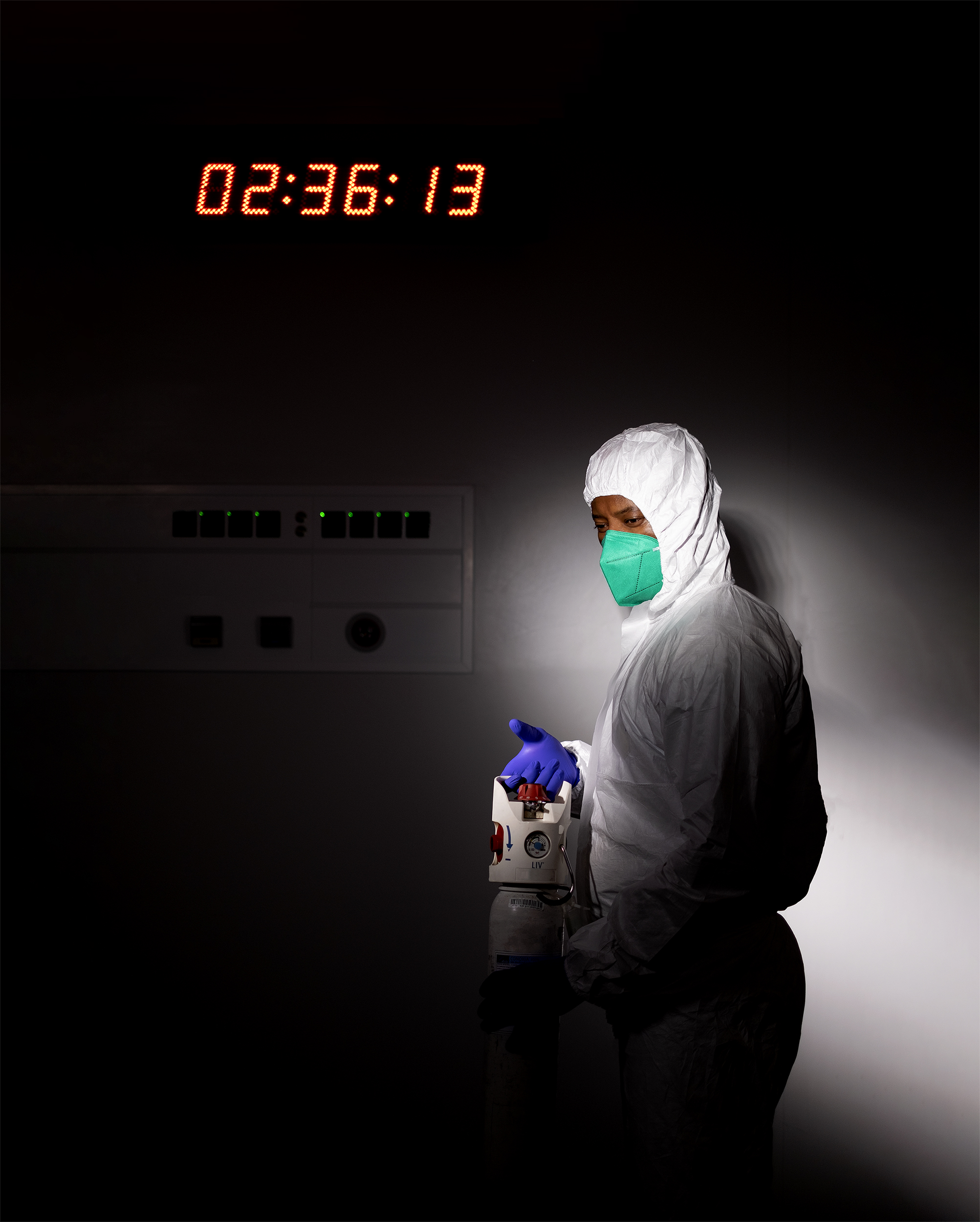 Enfermeira em ambiente escuro com equipamento de proteção individual branco segura garrafa de oxigénio.