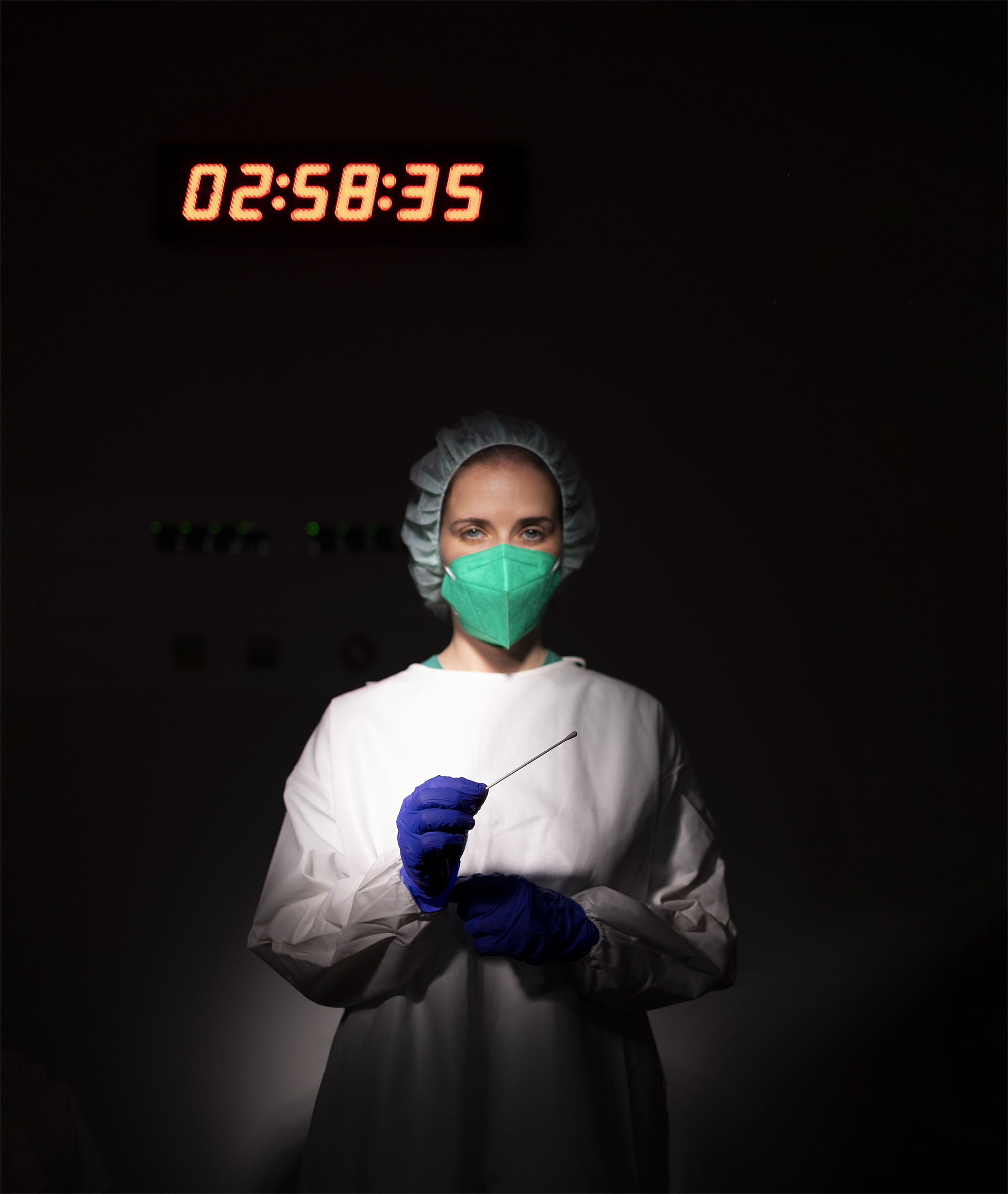 Enfermeira em ambiente escuro com face revelada, usa equipamento de proteção individual e segura zaragatoa com luvas.